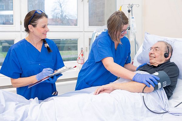 Das Bild zeigt zwei Pflegekräfte und einen Patienten bei der Blutdruckmessung vor der Dialyse