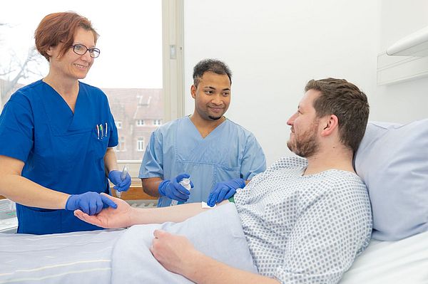 Das Bild zeigt zwei Pflegekräfte und einen Patienten bei der Blutentnahme