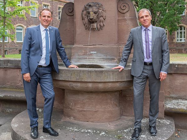 Das Bild zeigt unsere beiden Geschäftsführer Markus Heming und Prof. Michael Geißler vor dem Brunnen bei Haus A